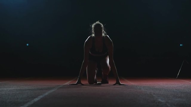 Female athlete on a dark background is preparing to run the cross-country sprint from the pads on the treadmill on a dark background