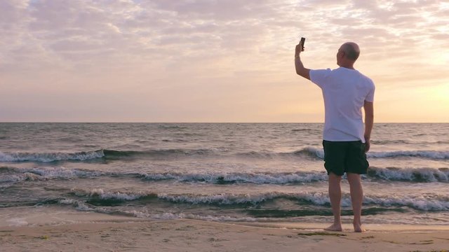 Adult man making selfie andmobile photo morning sunrise on sea beach