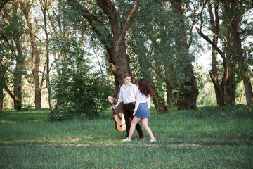 young couple walking in the forest and playing guitar, summer nature, bright sunlight, shadows and green leaves, romantic feelings