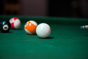 Sport billiard balls on green billiard table in pub. Player is about to hit the ball, focusing on his shot. On going billiard game. Competitive players trying to find out the winner of the round.