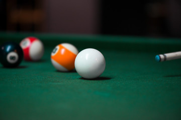 Sport billiard balls on green billiard table in pub. Player is about to hit the ball, focusing on his shot. On going billiard game. Competitive players trying to find out the winner of the round.