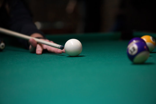 Sport billiard balls on green billiard table in pub. Player is about to hit the ball, focusing on his shot. On going billiard game. Competitive players trying to find out the winner of the round.