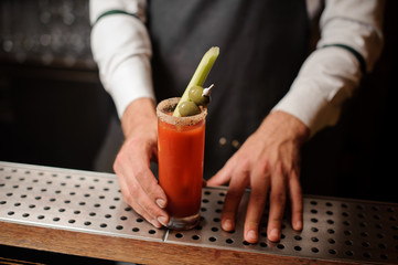 Bartender serving a bloody mary cocktail with two olives on the skewer and celery