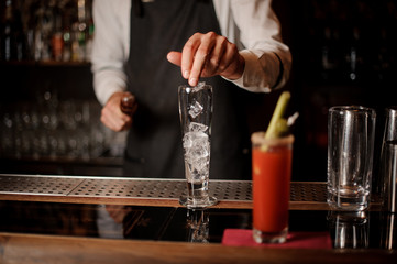 Fototapeta na wymiar Bartenter adding ice into an empty cocktail glass
