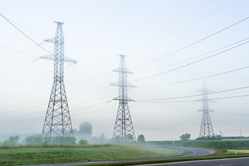 High voltage transmission towers in meadow at orange sunset 
