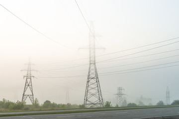 High voltage transmission tower in meadow at foggy morning 

