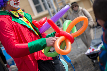 A freelance clown creating balloon animals and different shapes at outdoor festival in city center....