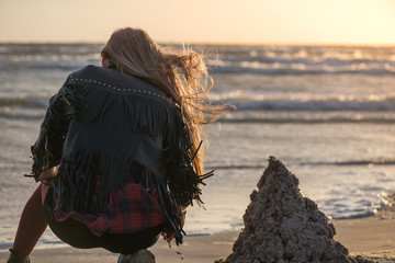 Young woman building and making sand castle next to sea. Calm, relaxing and romantic evening during...