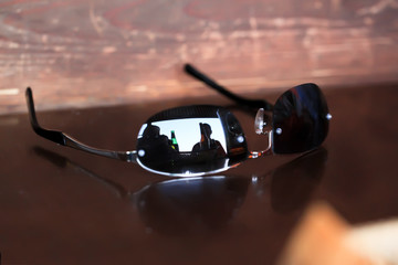 Reflection of beer bottles in sunglasses lying on a wooden table.