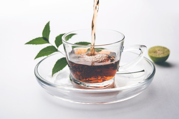 pouring Neem tea in transparent glass cup with saucer over white background. Popular Ayurvedic medicine from India