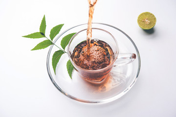 pouring Neem tea in transparent glass cup with saucer over white background. Popular Ayurvedic medicine from India