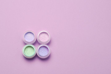 Obraz na płótnie Canvas Cosmetics. Makeup. Jars with crumbly bright shadows, glitter. Pink, green, lilac colors on lilac background. Closeup. Space for text or design.