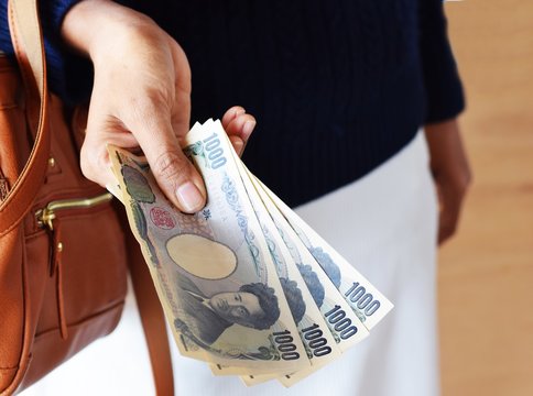 woman hand with Japanese banknotes and brown leather handbag on wood background with copy space