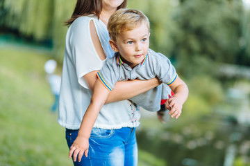 Happy family in the park evening light. Mother hold son on hands. Mom throws her blond baby boy...
