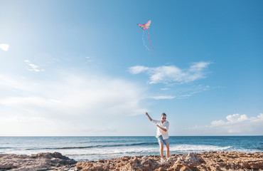 Young woman in a white shirt and shorts launches a kite on the seashore, travel and vacation concept, the joy of life