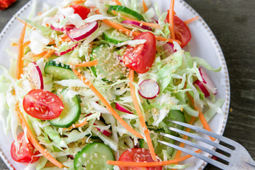 Fresh dietary salad of cucumbers, tomatoes, cabbages, radishes, carrots with sesame seeds, olive oil, garlic and herbs. Healthy meal. Detox and vegetarian concept.