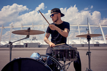 young tattooed drummer in sunglasses playing drums on street