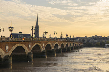 Naklejka premium Pont de Pierre stone bridge on the river garonne in Bordeaux, France at sunset with the st michel church in the background
