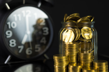 Coins stacks with coin in glass jar bottle and alarm clock in dark room, business and finance concept.
