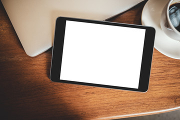 Top view mockup image of a black tablet pc with blank desktop white screen with laptop and coffee cup on wooden table