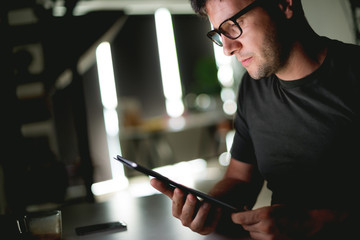 Young caucasian man sitting in front of computer, holding digital tablet