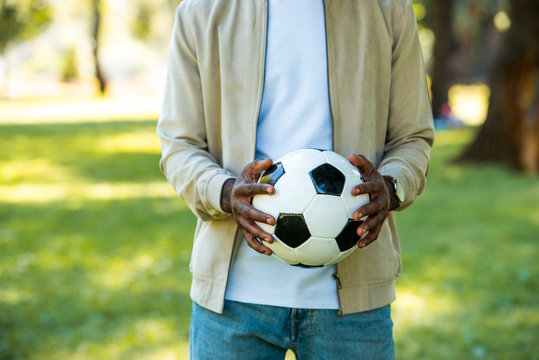 cropped image of african american man holding football ball in hands in park