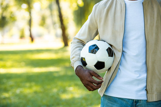 cropped image of african american man holding football ball in park