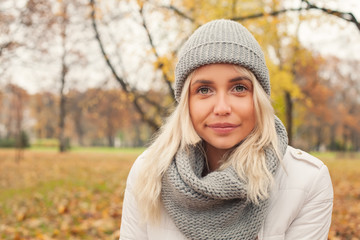Autumn woman in grey knitted hat and scarf outdoors. Cute girl walking in fall park