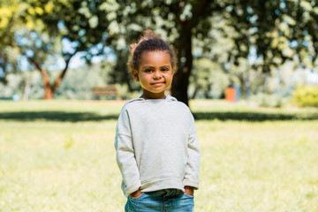 Fototapeta premium adorable african american kid in jeans and sweater looking at camera in park