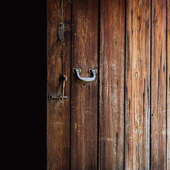 Opened old weathered wooden door with polished metal handle, steel latch and wooden bolt hanging on a string