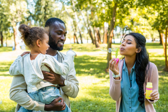 african american mother blowing soap bubbles in park