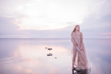 A girl in a weightless light fabric of pastel tones in the water of a calm pond with a reflection...