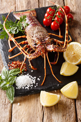 Raw spiny lobster with spices, vegetables ingredients close-up on a black board on a table. Vertical