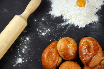 Baked buns on a table with a rolling pin, flour and egg