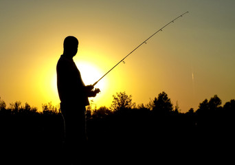 silhouette of fisherman with fishing rod on sunset background