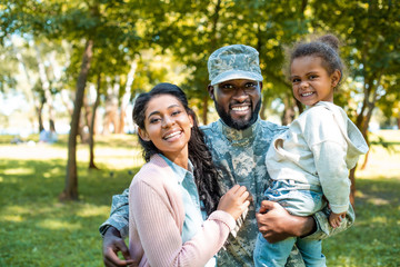 Happy African American soldier in military uniform looking at camera with family in park - Powered by Adobe
