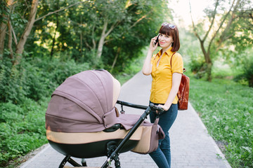 Fototapeta na wymiar Full length portrait of a mother talking on the phone with a stroller. Young mom