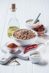 Close up view of raw chickpeas, spices, chili pepper, dried tomatoes and olive oil (hummus ingredients) on wooden tabletop