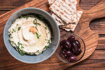 top view of olives, pita bread and hummus with parsley and chickpeas in bowl on cutting  board wooden surface