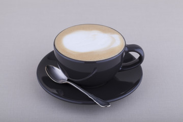 Black cup of cappuccino with foam on textile background