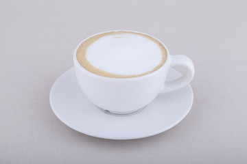 White cup of cappuccino with foam on textile background