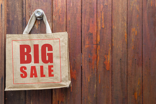 Big Sale Logo On Jute Shopping Bag Hanging Over Old Wooden Door Background, Business Object