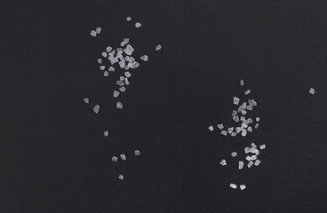 Handful of sea salt scattered on a black background top view - obrazy, fototapety, plakaty