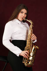 Fototapeta na wymiar Young girl with saxophone in studio on dark background