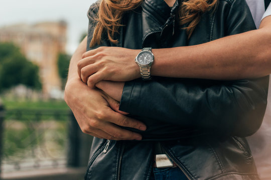 The Guy Is Behind And Hugs The Girl, Hands Together.on The Hand Of A Guy Wearing Watch.date.male Hands, Hands Close-up, Embrace Another Person In A Black Jacket. On The Hands Of A Watch.