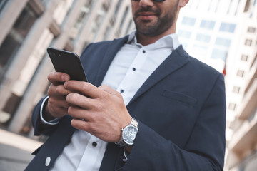 Confident businessman. Businessman on city street checking time and using smart phone. Focus is on hands