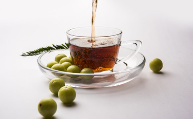 pouring amla Tea or Avla Chai in transparent glass cup with saucer over white or black background. Popular Ayurvedic medicine from India