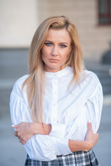 pensive young blond woman on building background with columns. sad girl in a white blouse