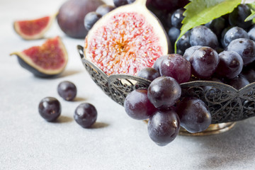 Fresh figs and black grapes with leaves in a plate on a grey table selective focus. Copy space
