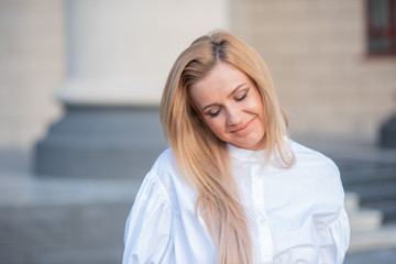 portrait of a blonde on a building background with columns. beautiful blonde in a white blouse smiling